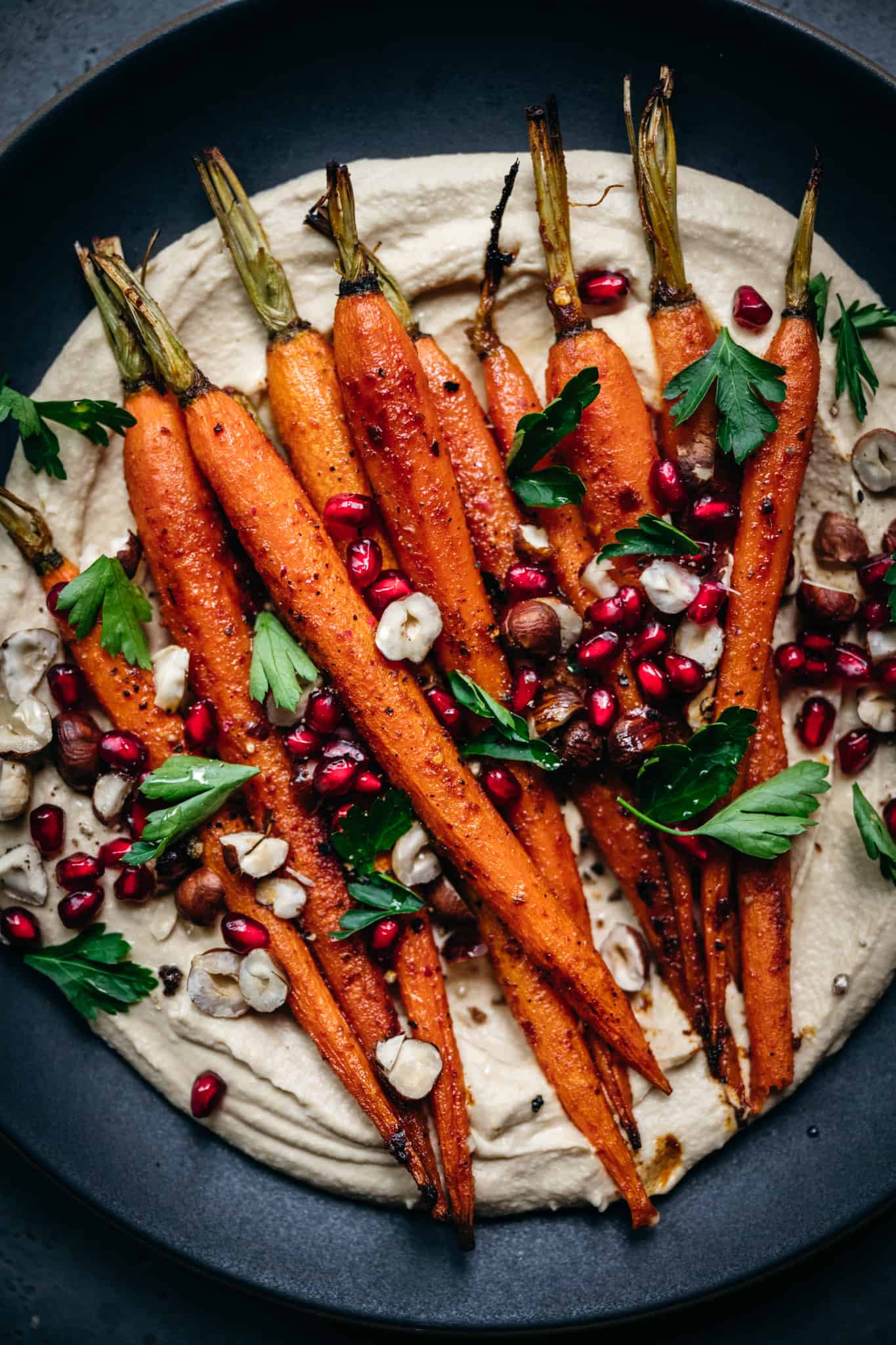 close up overhead of harissa roasted carrots on pumpkin hummus with pomegranate seeds