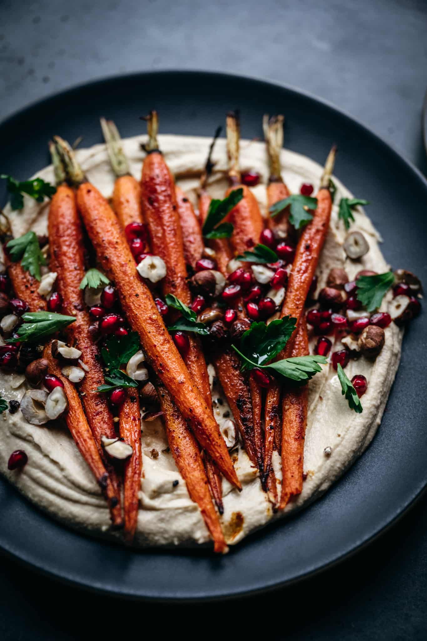 close up overhead of vegan harissa roasted carrots with pomegranate seeds and tahini dressing