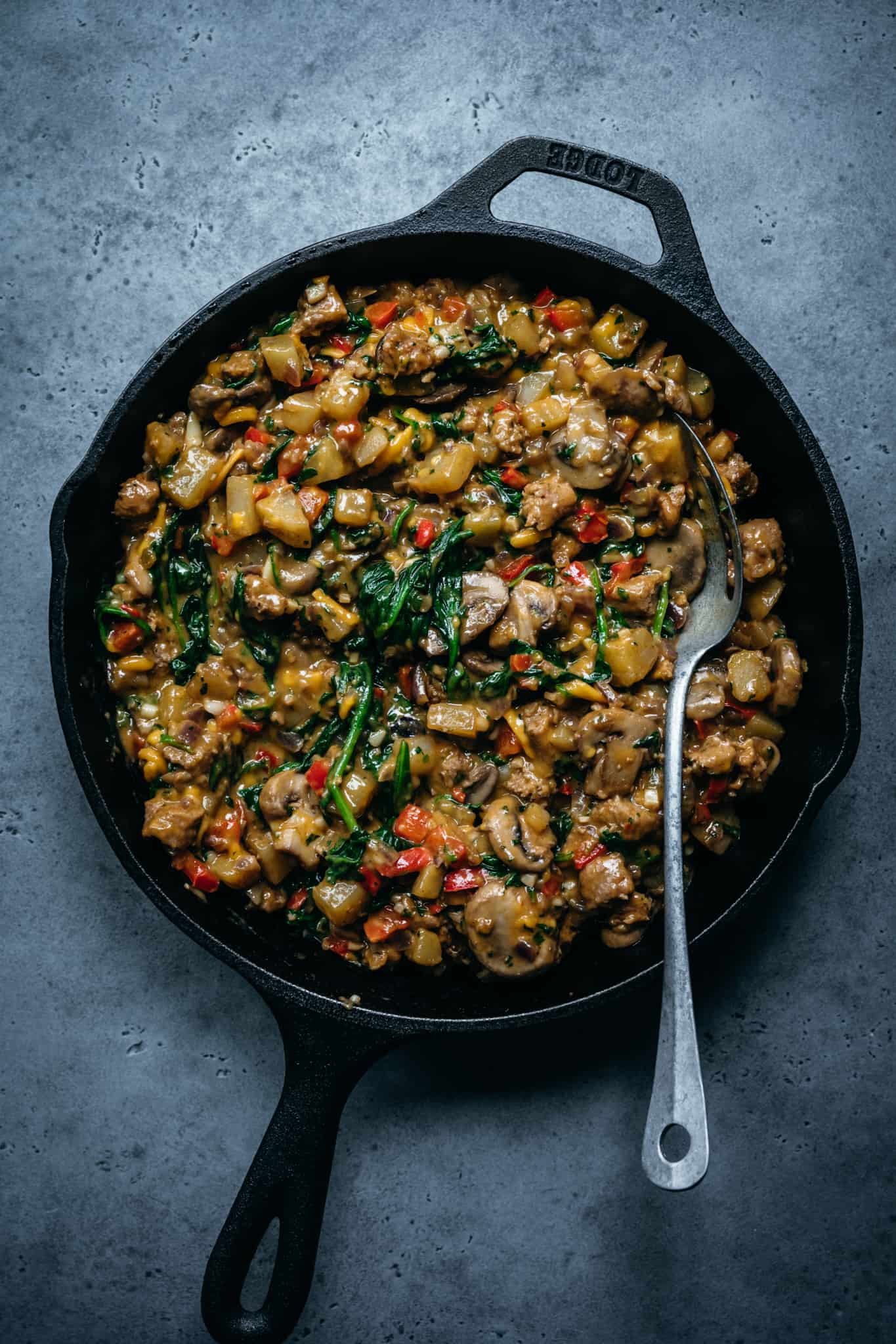 overhead of the cooked vegetables and vegan sausages in a cast iron skillet