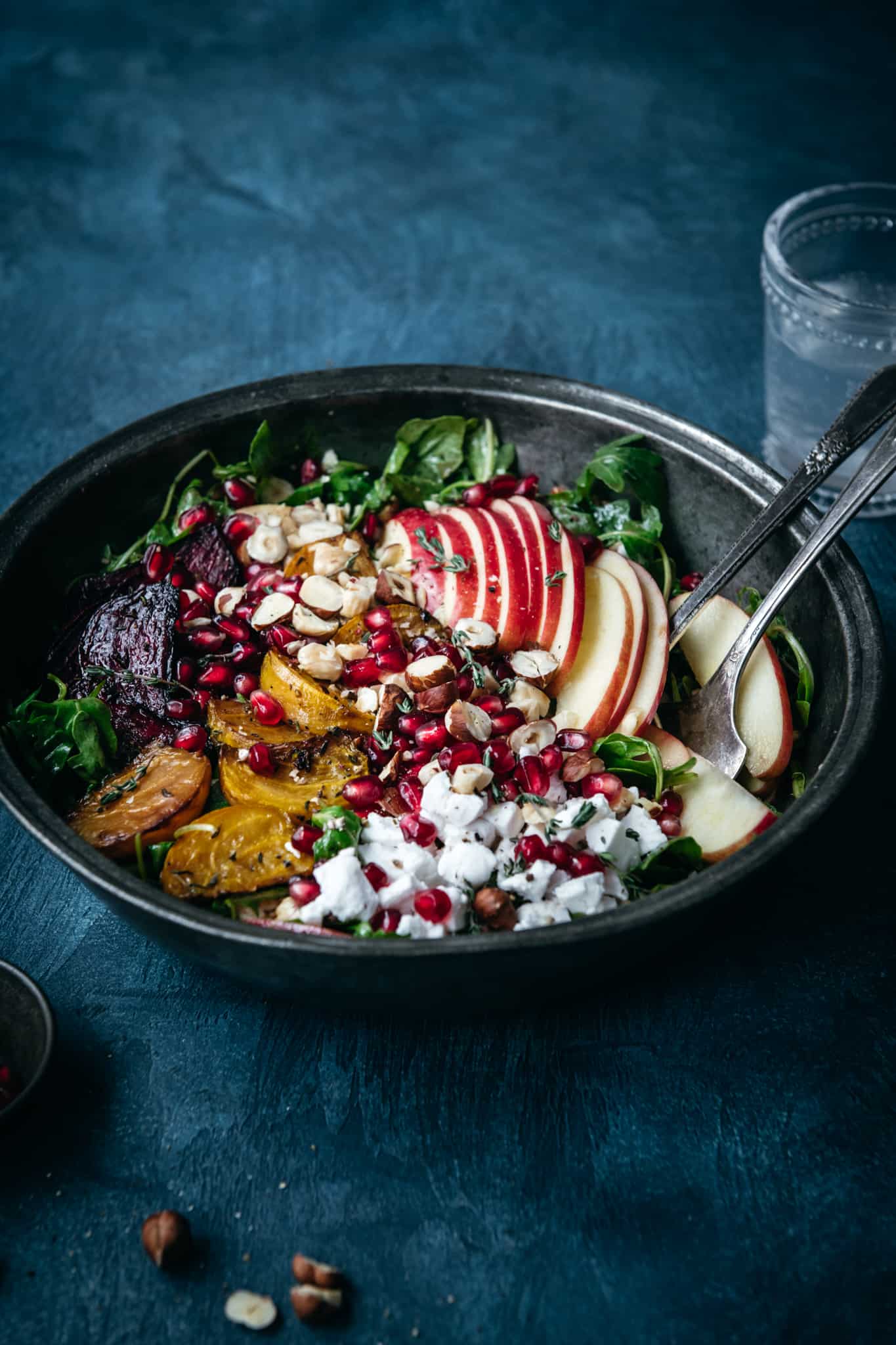 side view of roasted beet kale salad with hazelnuts, apple, pomegranate and feta in a large salad bowl