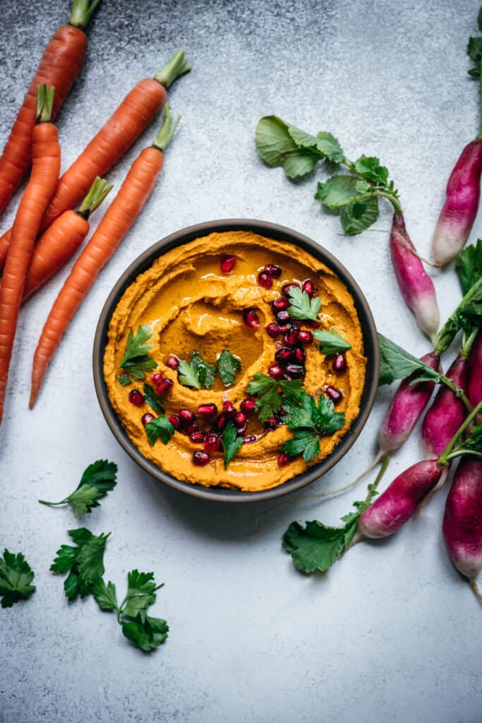overhead of vegan roasted carrot dip on a light background with carrots and radishes