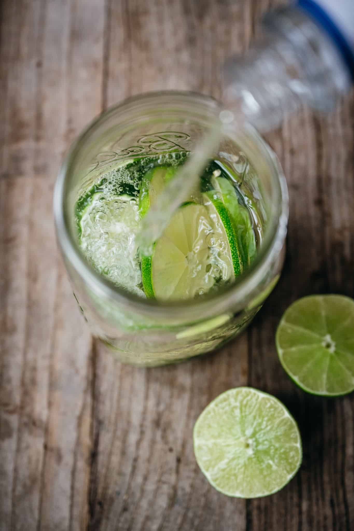 pouring tequila into jar with limes and jalapeños