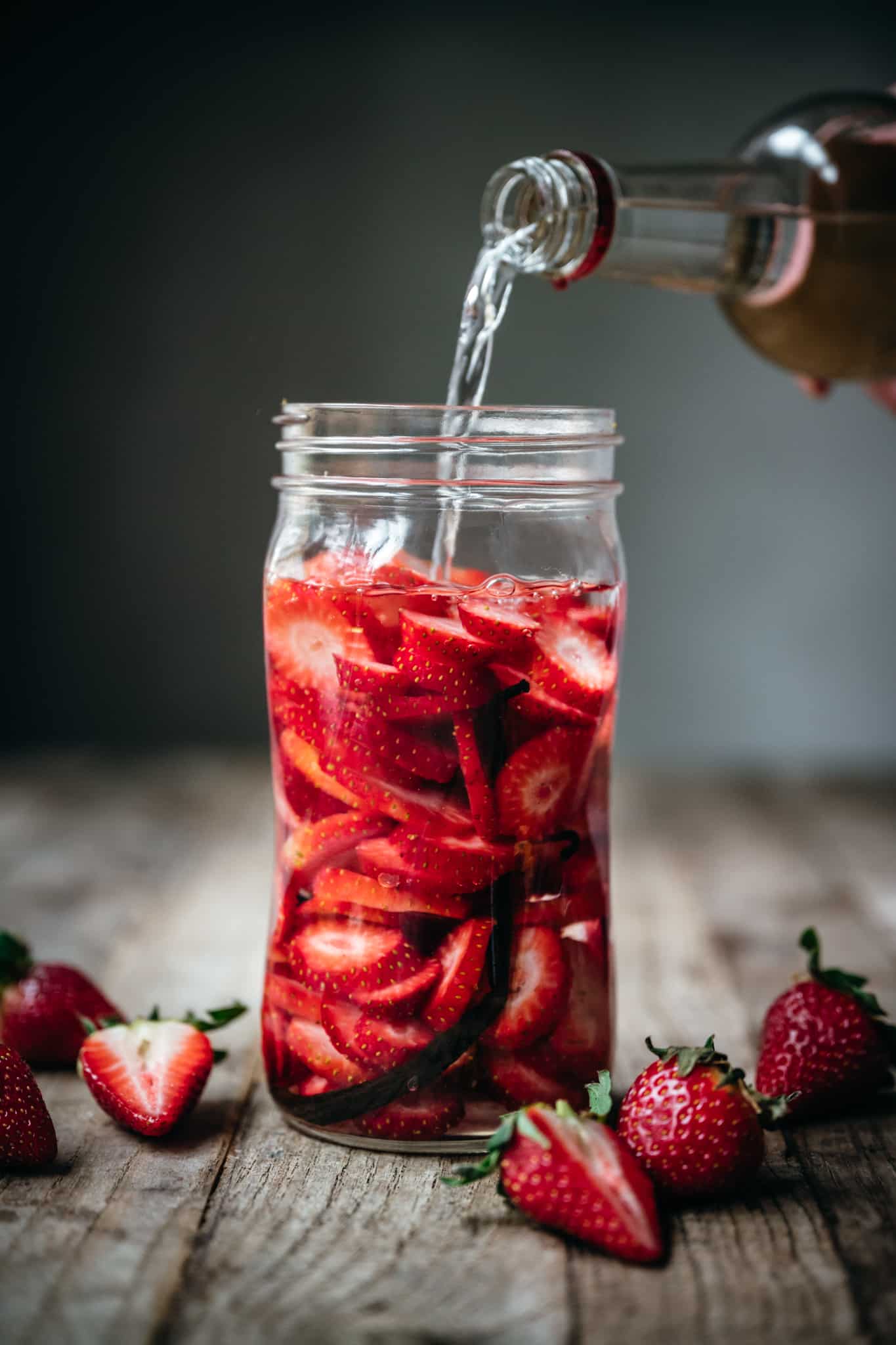 pouring vodka into jar with strawberries and vanilla