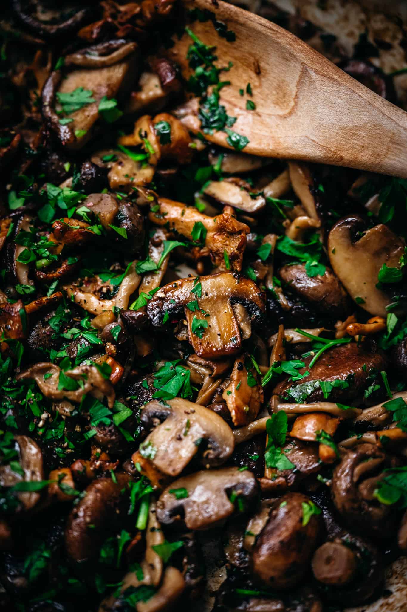 clsoe up overhead of panseared wild mushrooms in a skillet with a wooden spoon