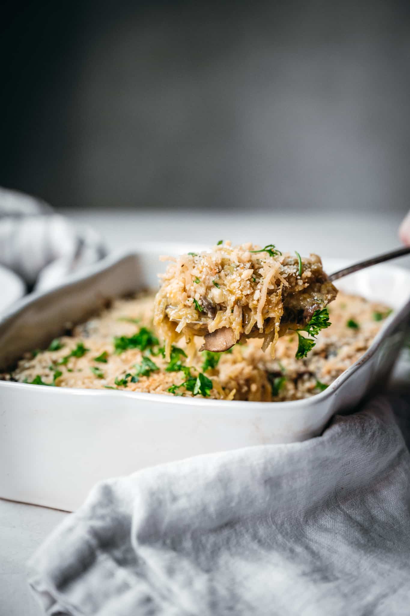 side view of a scoop being taken out of the vegan spaghetti squash casserole in a white serving dish 