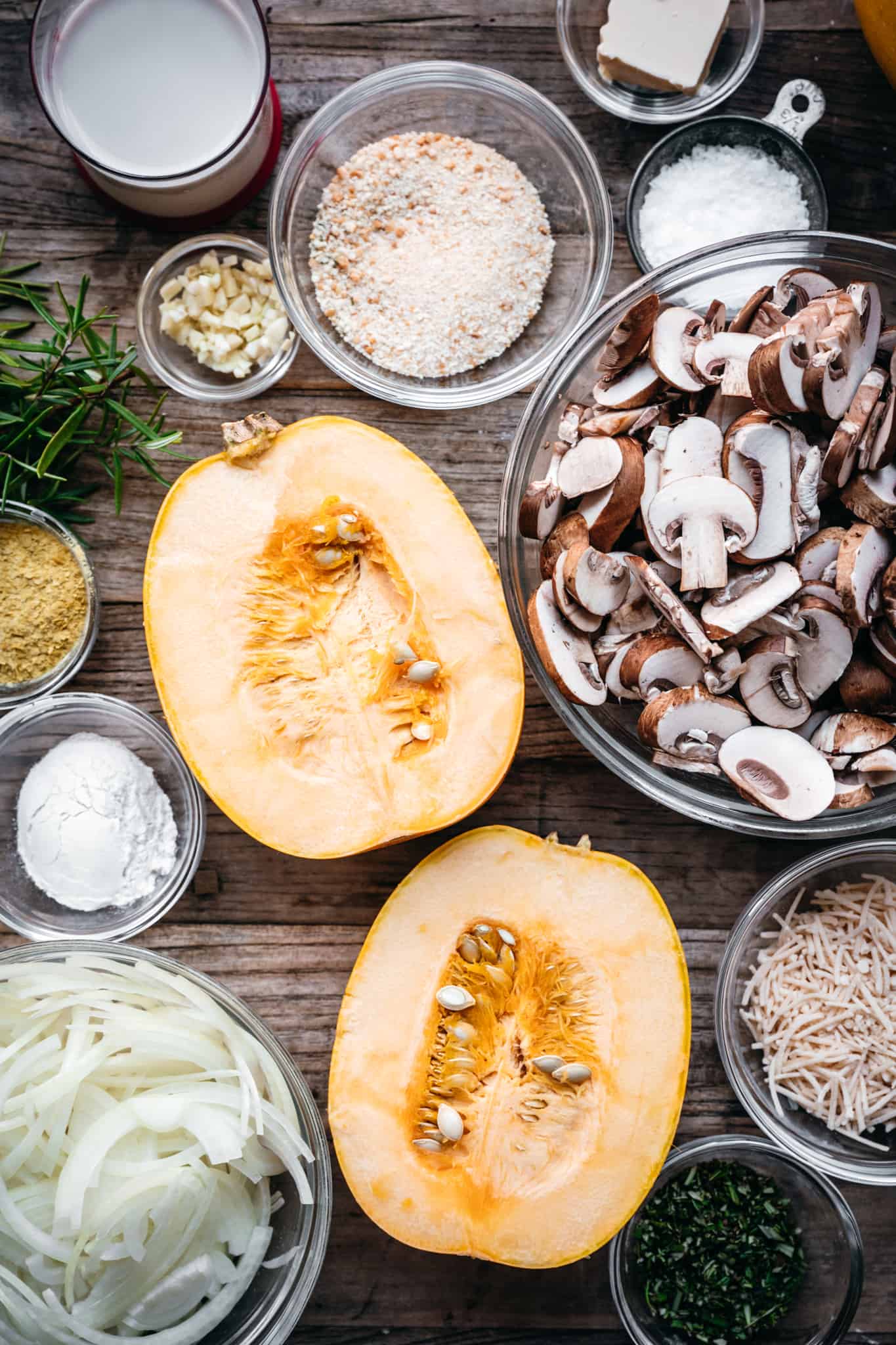 overhead of a spaghetti sqasuh, mixed mushrooms, and other ingredients for vegan casserole in small bowls on a wooden background