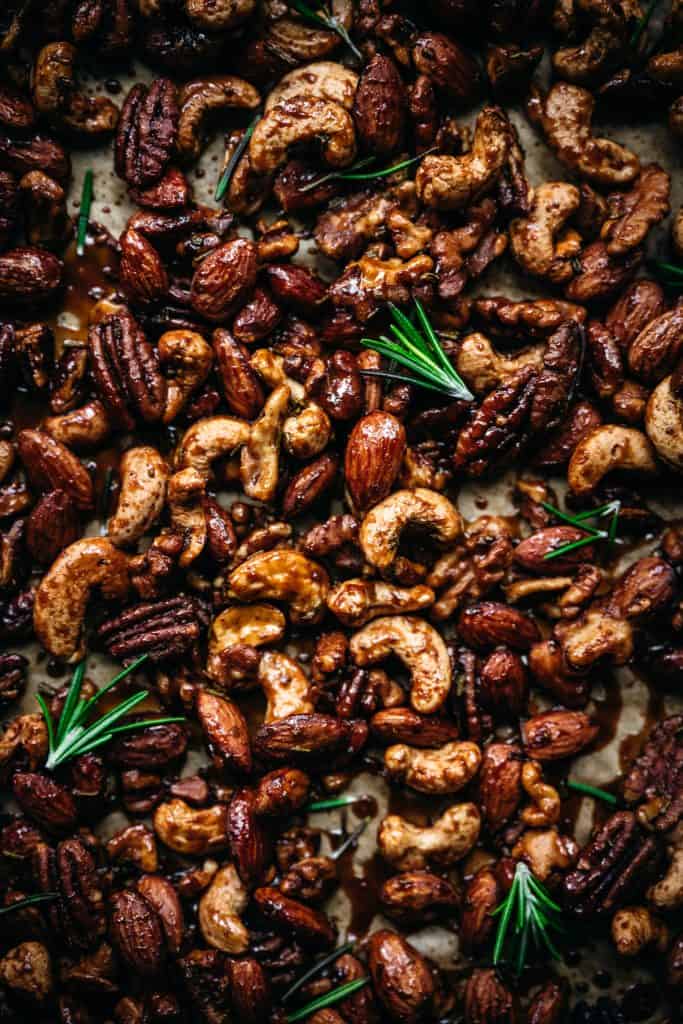 close up overhead of vegan spiced nuts on a baking sheet with fresh rosemary sprigs