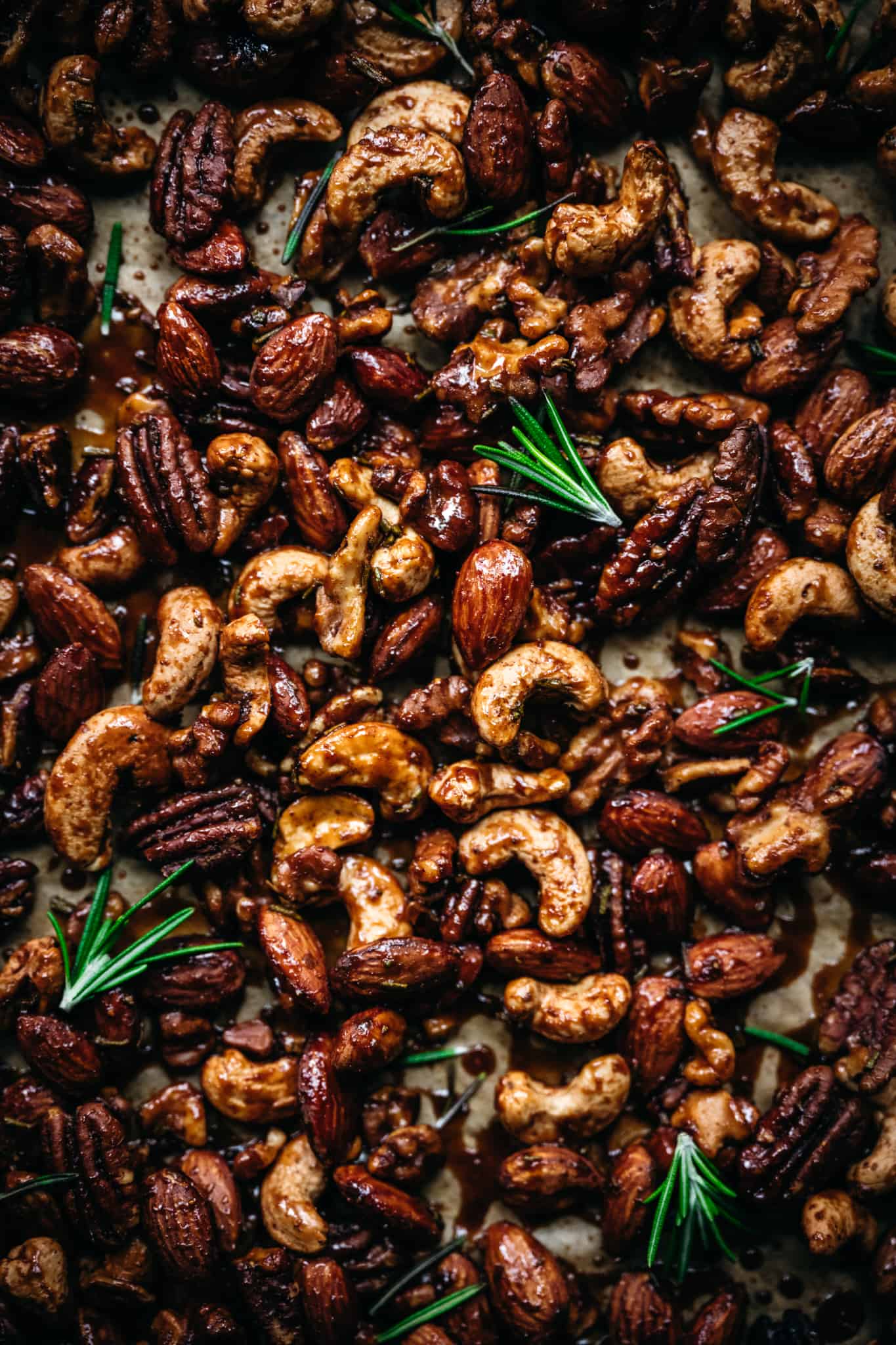 close up overhead of vegan spiced nuts on a baking sheet with fresh rosemary sprigs