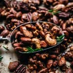 close up of mixed spiced nuts on a baking sheet with a spoon