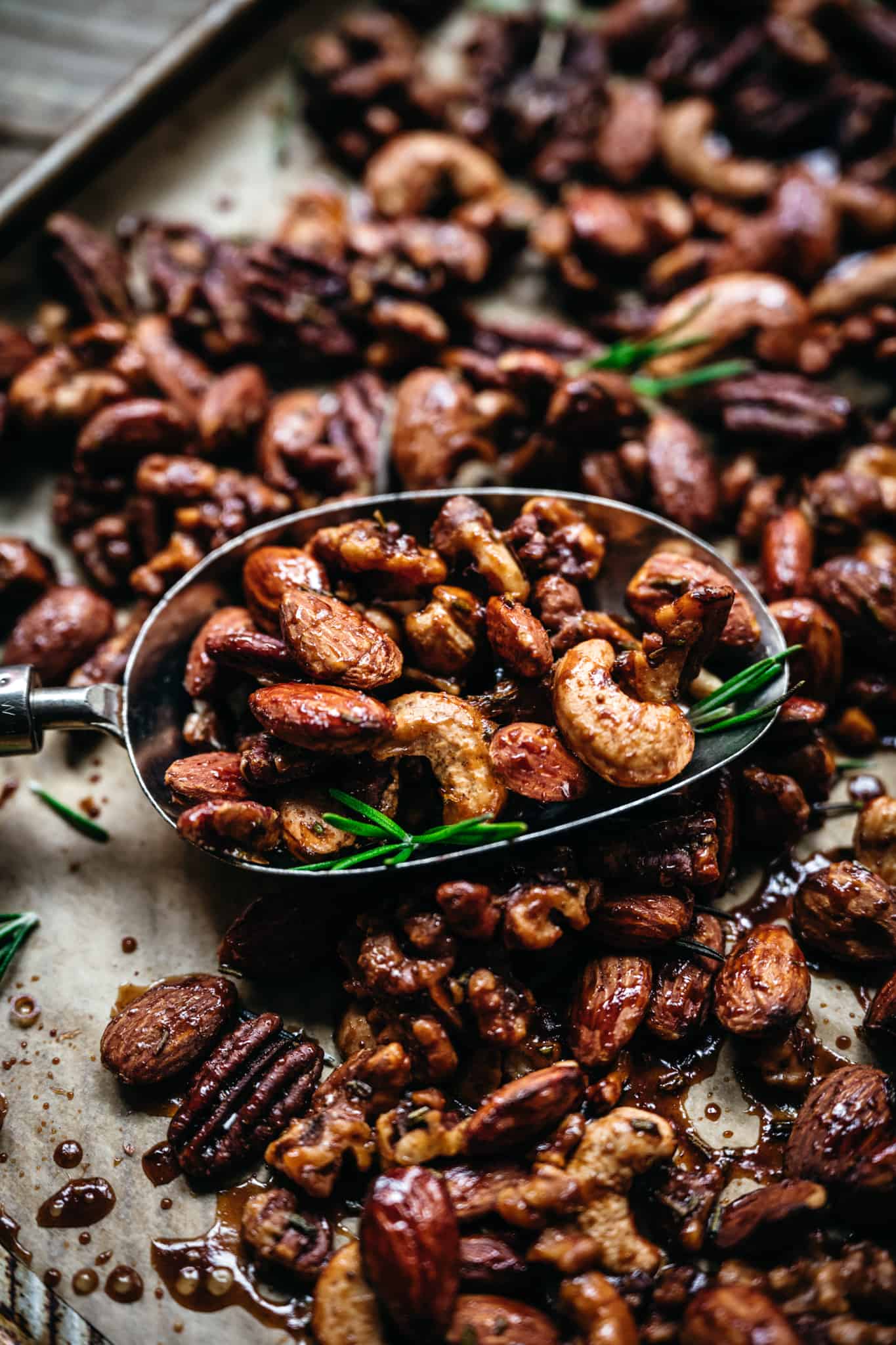 close up of mixed spiced nuts on a baking sheet with a spoon