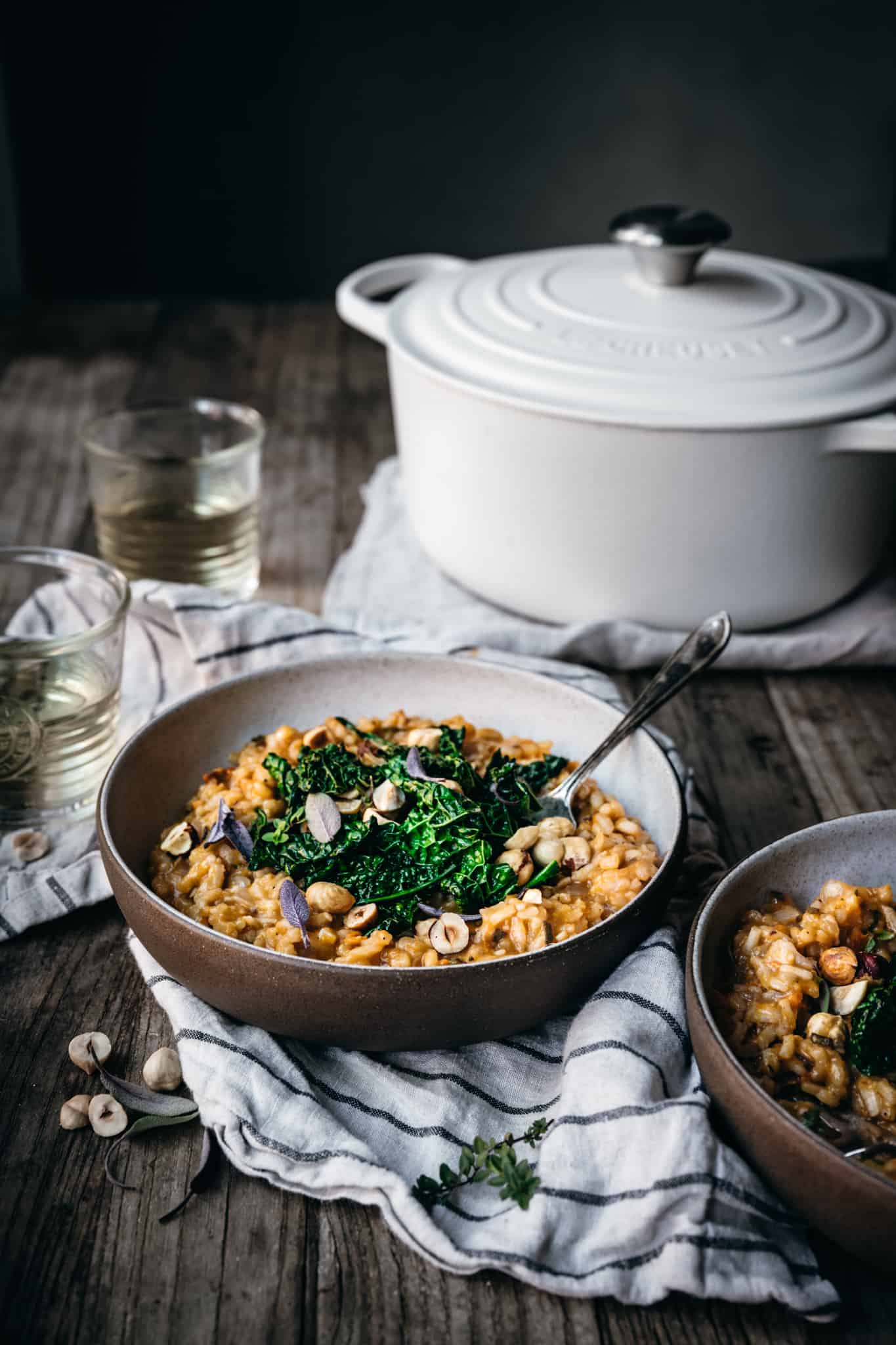 side view of two bowls of risotto on a wood table with wine