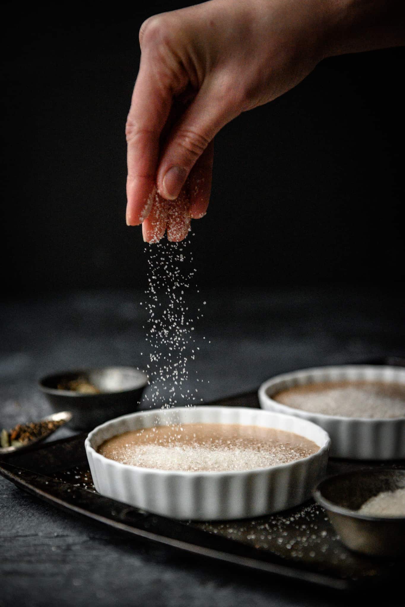 person sprinkling sugar on top of vegan chai infused creme brulee