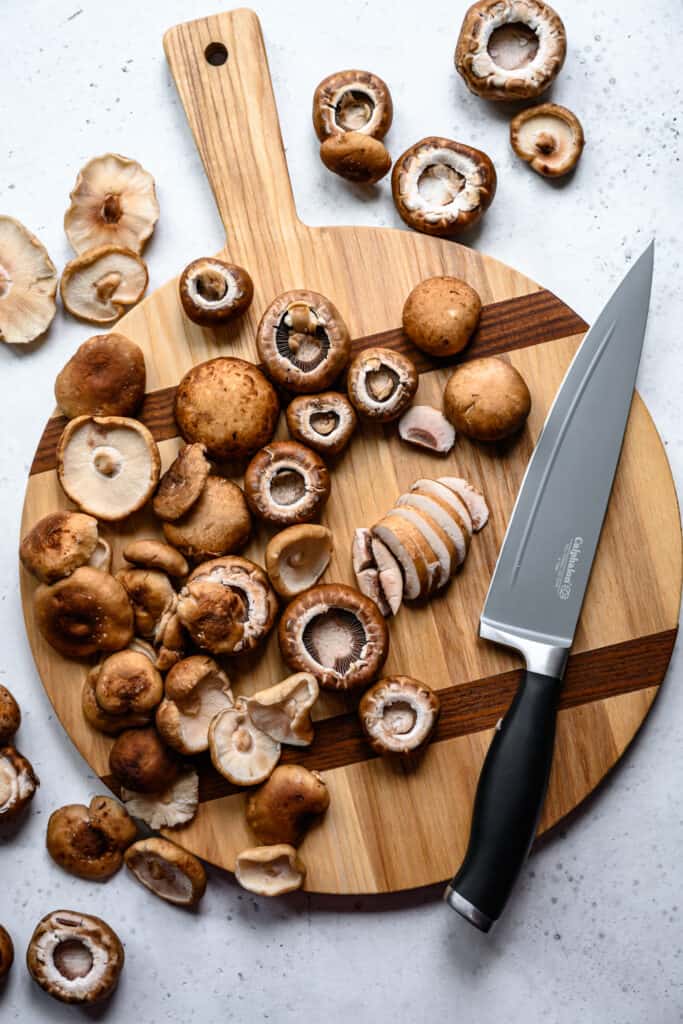 overhead view of button mushrooms on wood cutting board with knife