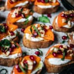 close up overhead of goat cheese crostini with persimmon and pomegranate seeds