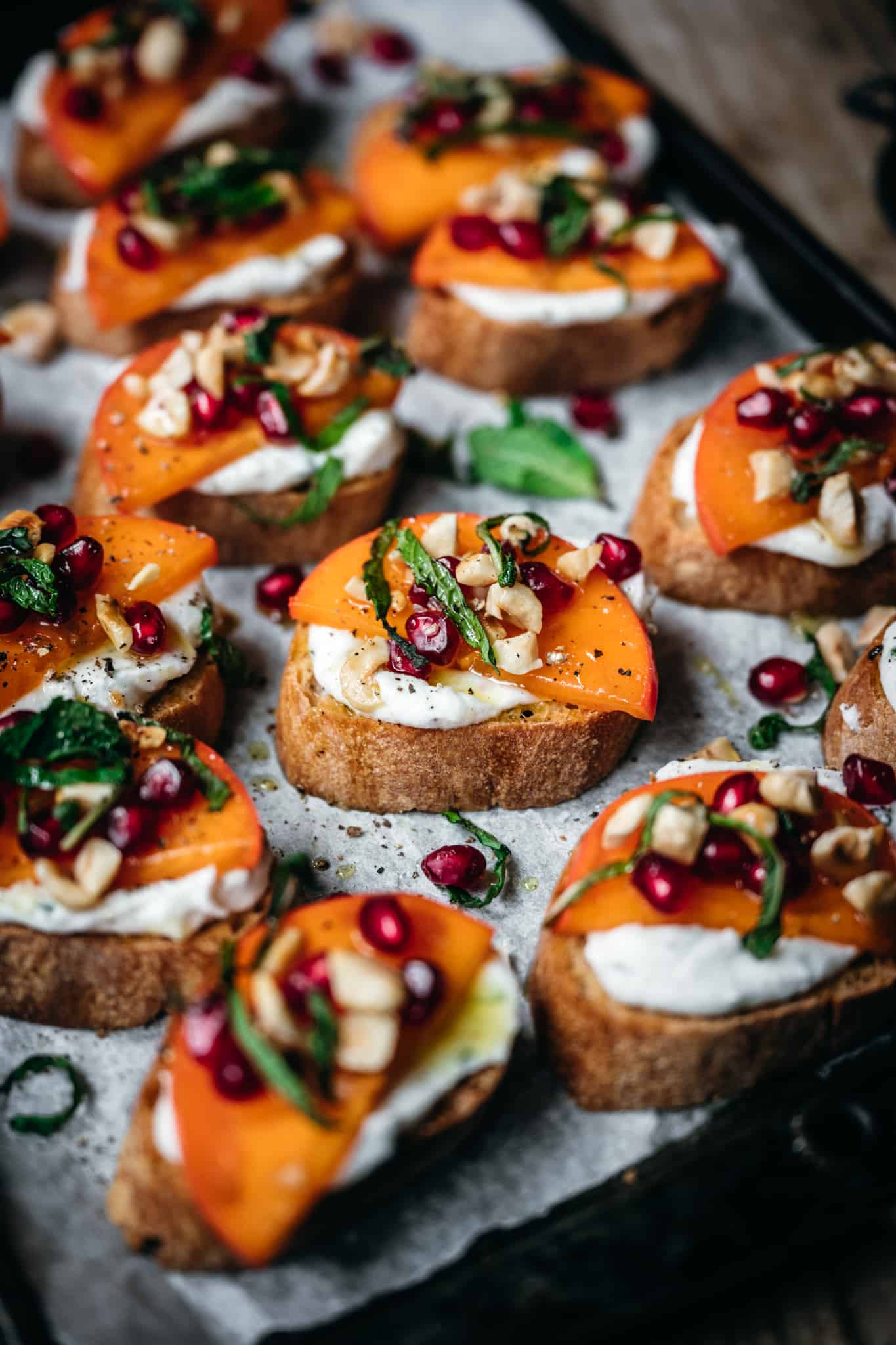 close up overhead of goat cheese crostini with persimmon and pomegranate seeds
