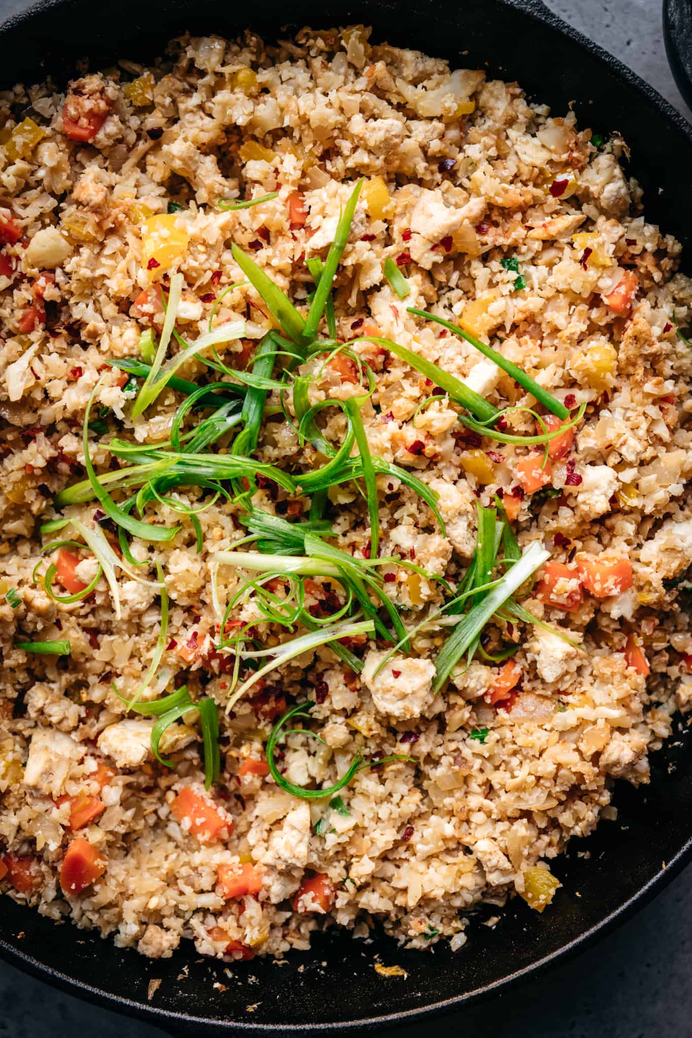 close up overhead of vegan cauliflower fried rice in a cast iron skillet with scallions on top