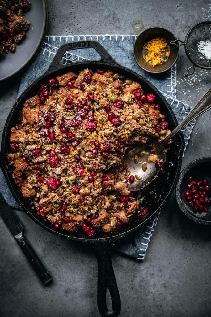overhead view of gluten free cranberry cardamom bread pudding in skillet with serving spoon
