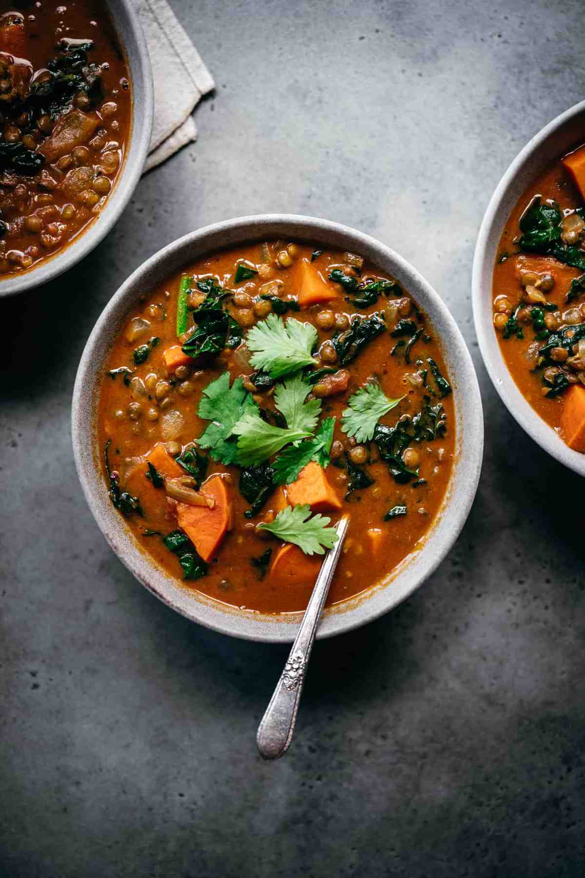 overhead view of lentil sweet potato curry soup in grey bowl with cilantro garnish