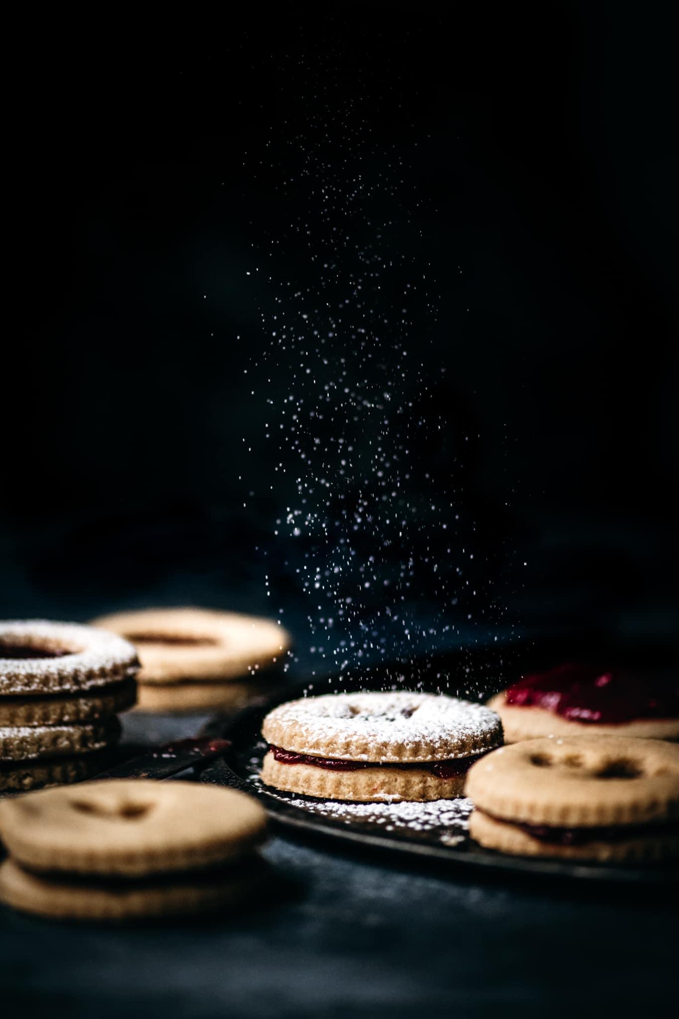 side view of dusting powdered sugar onto homemade linzer cookies