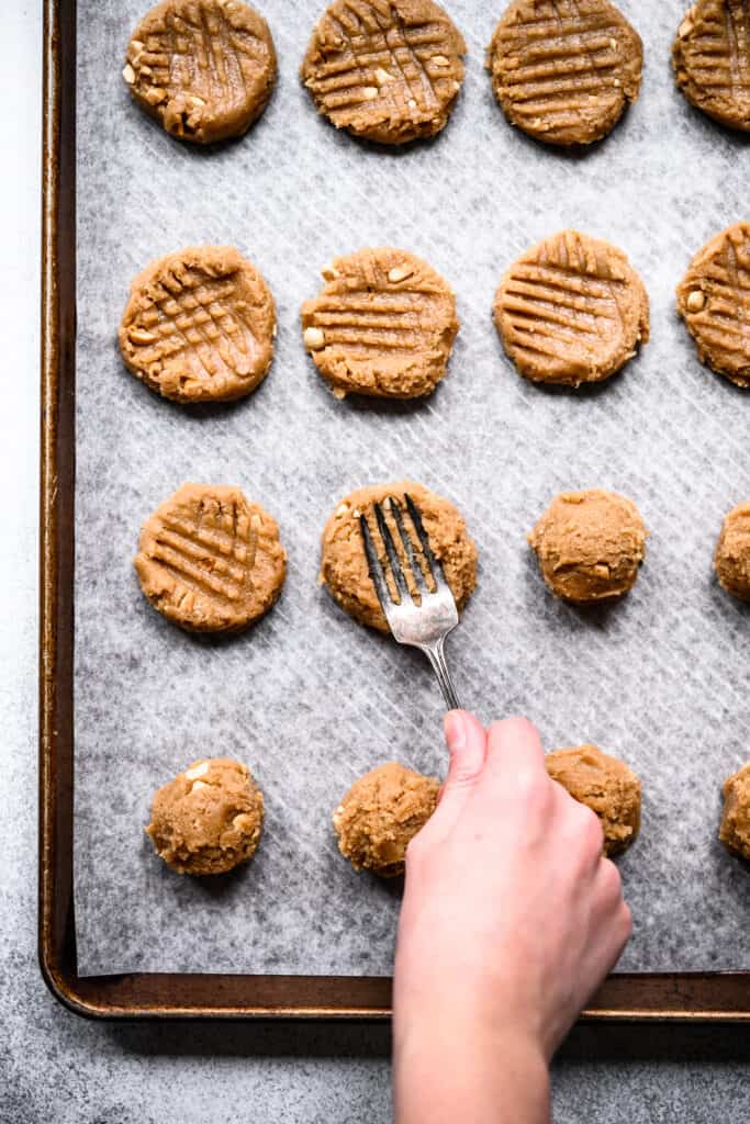 person using fork to flatten peanut butter cookie dough