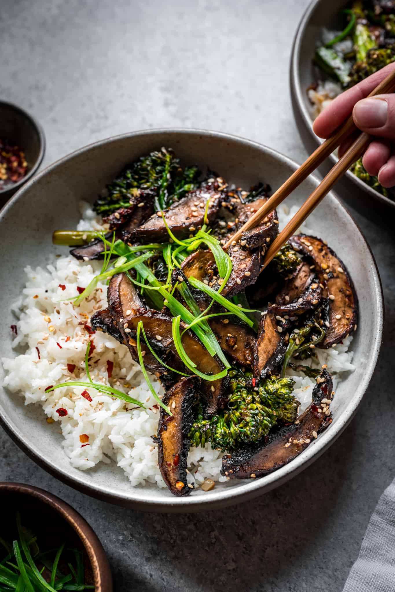 45 degree overhead of someone taking a bite of vegan teriyaki mushroom bowls