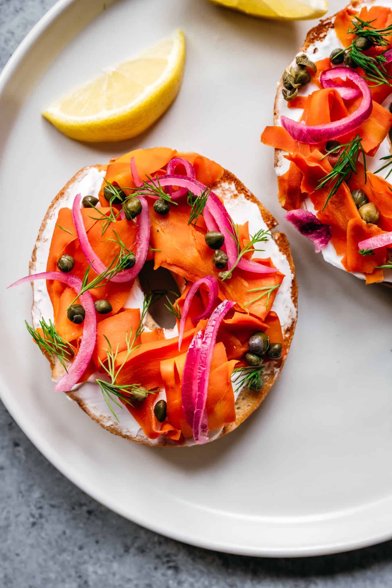 close up of a bagel with cream cheese, carrot lox, pickled red onions, capers and lemons lices