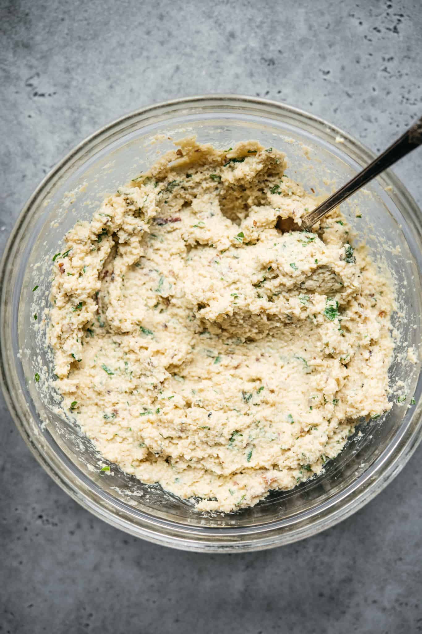 overhead of vegan cheese mixture in a glass mixing bowl with a spoon