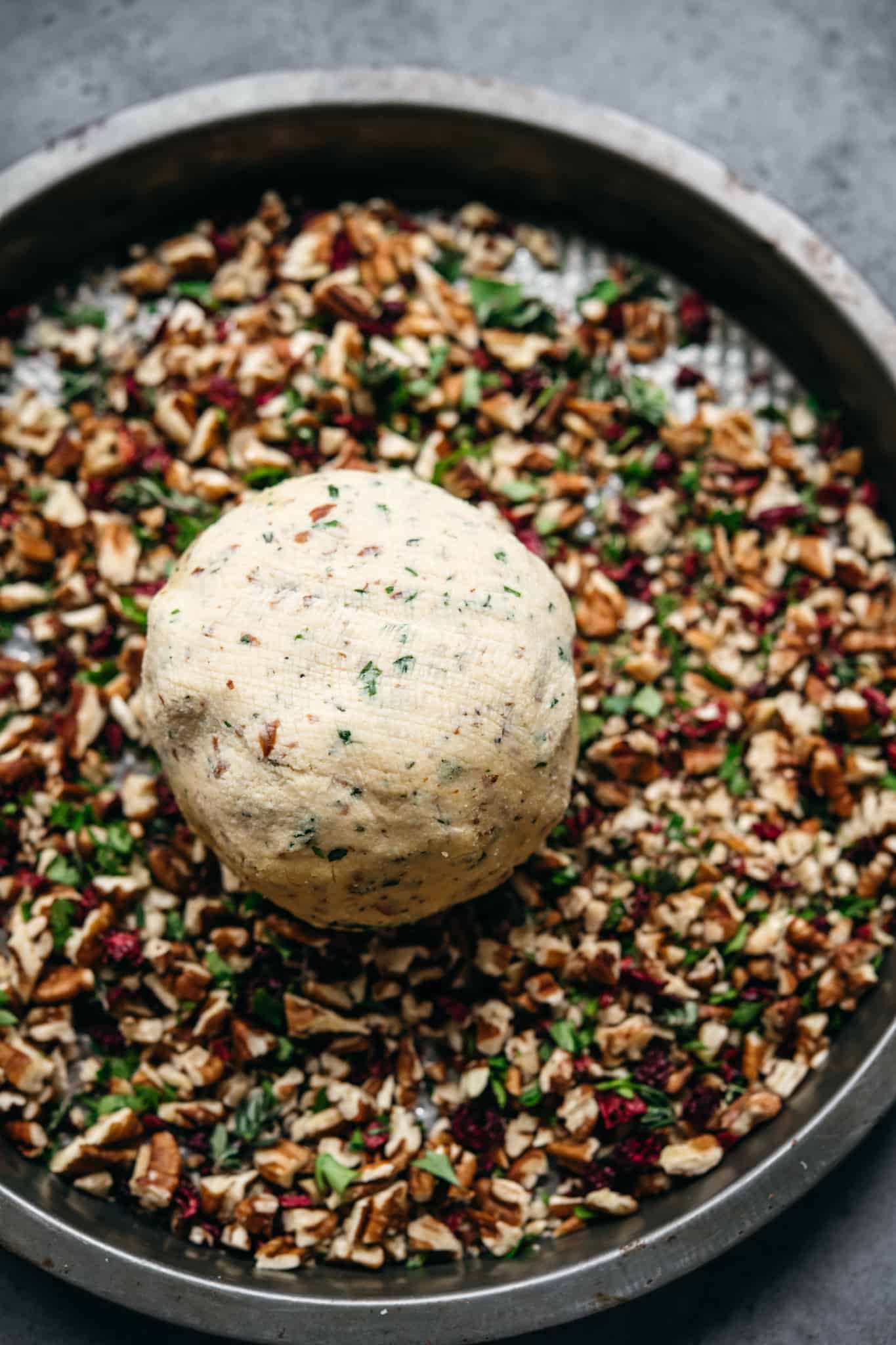 overhead of a vegan cheese ball on a plate of nut coating before it's covered