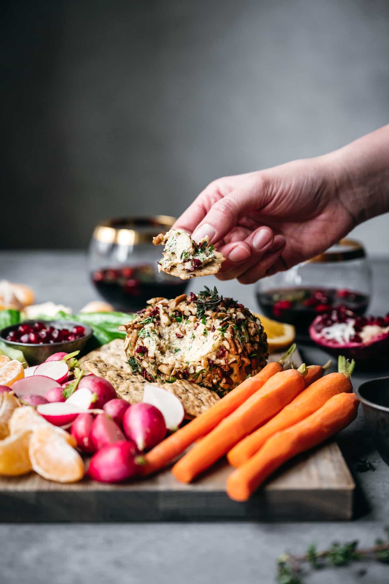 side view of a vegan cheese ball with vegetable cruidite and someone taking a bite