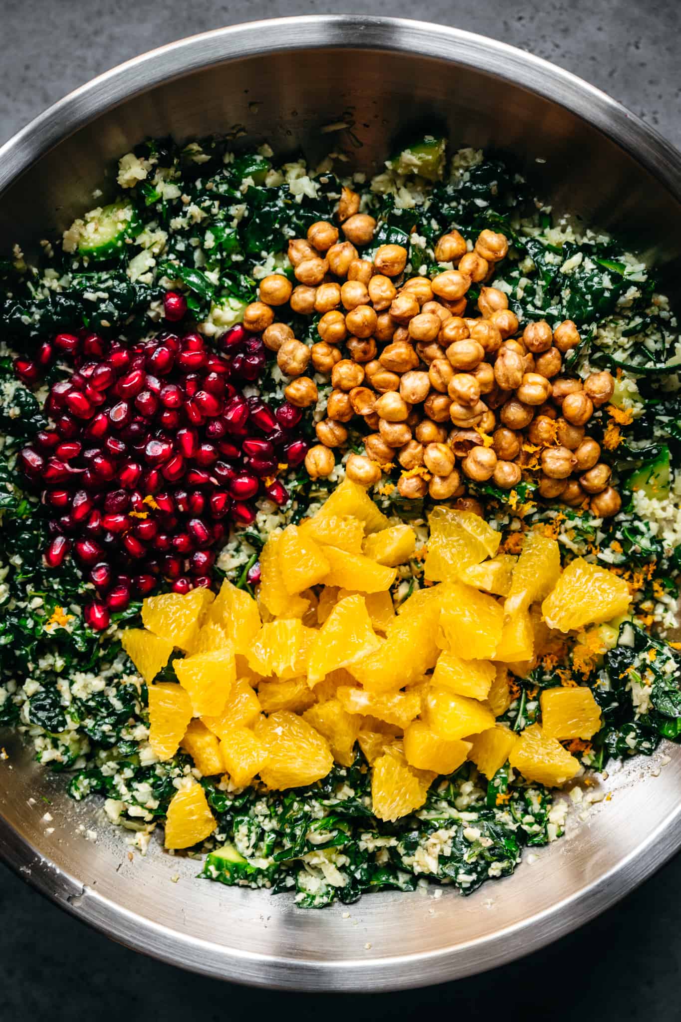 overhead view of cauliflower kale salad in mixing bowl with oranges, pomegranate and chickpeas