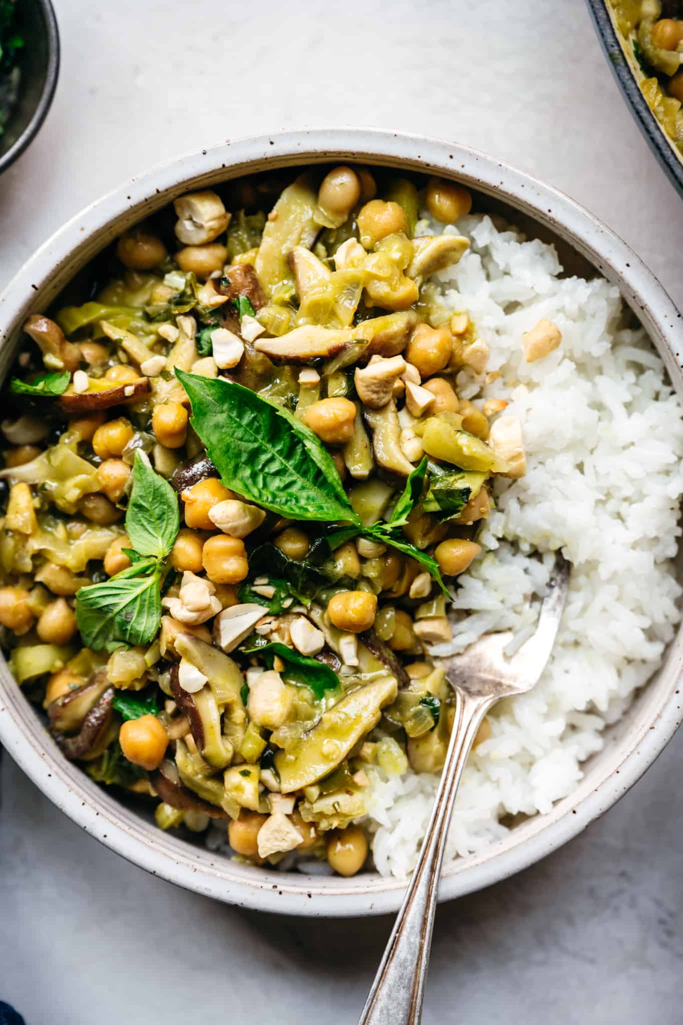 vegan green curry with chickpeas and mushrooms served over white rice in bowl 