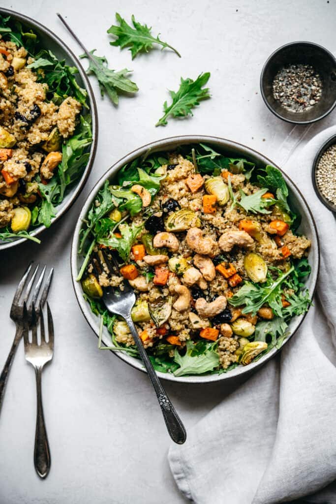 overhead view of two bowls of quinoa salad with roasted vegetables on white background