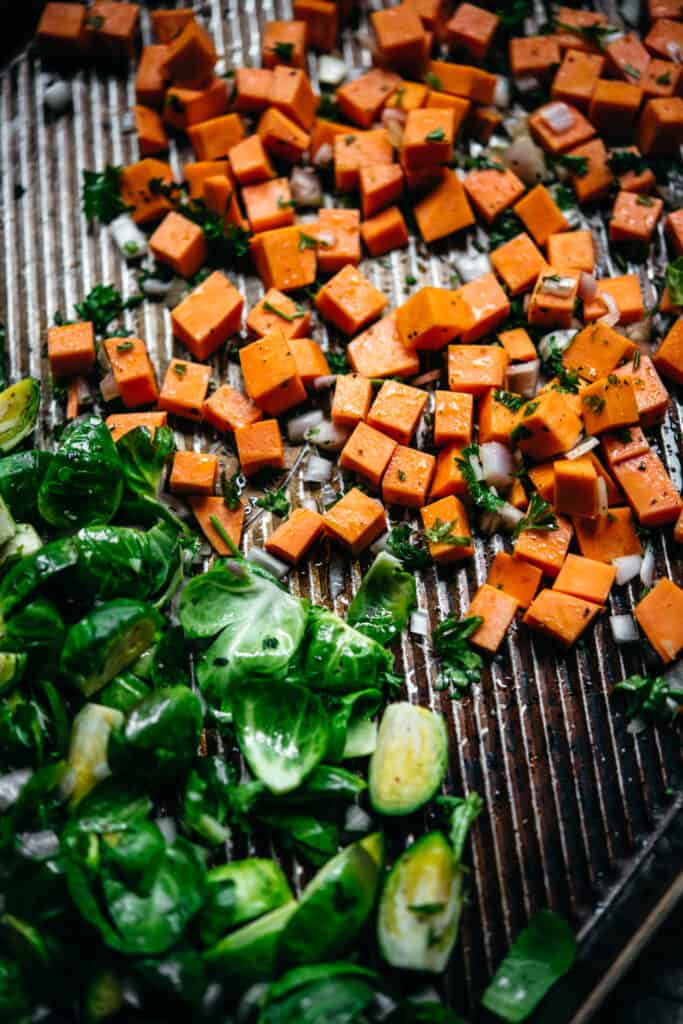 close up view of diced sweet potato and brussels sprouts on a sheet pan before roasting