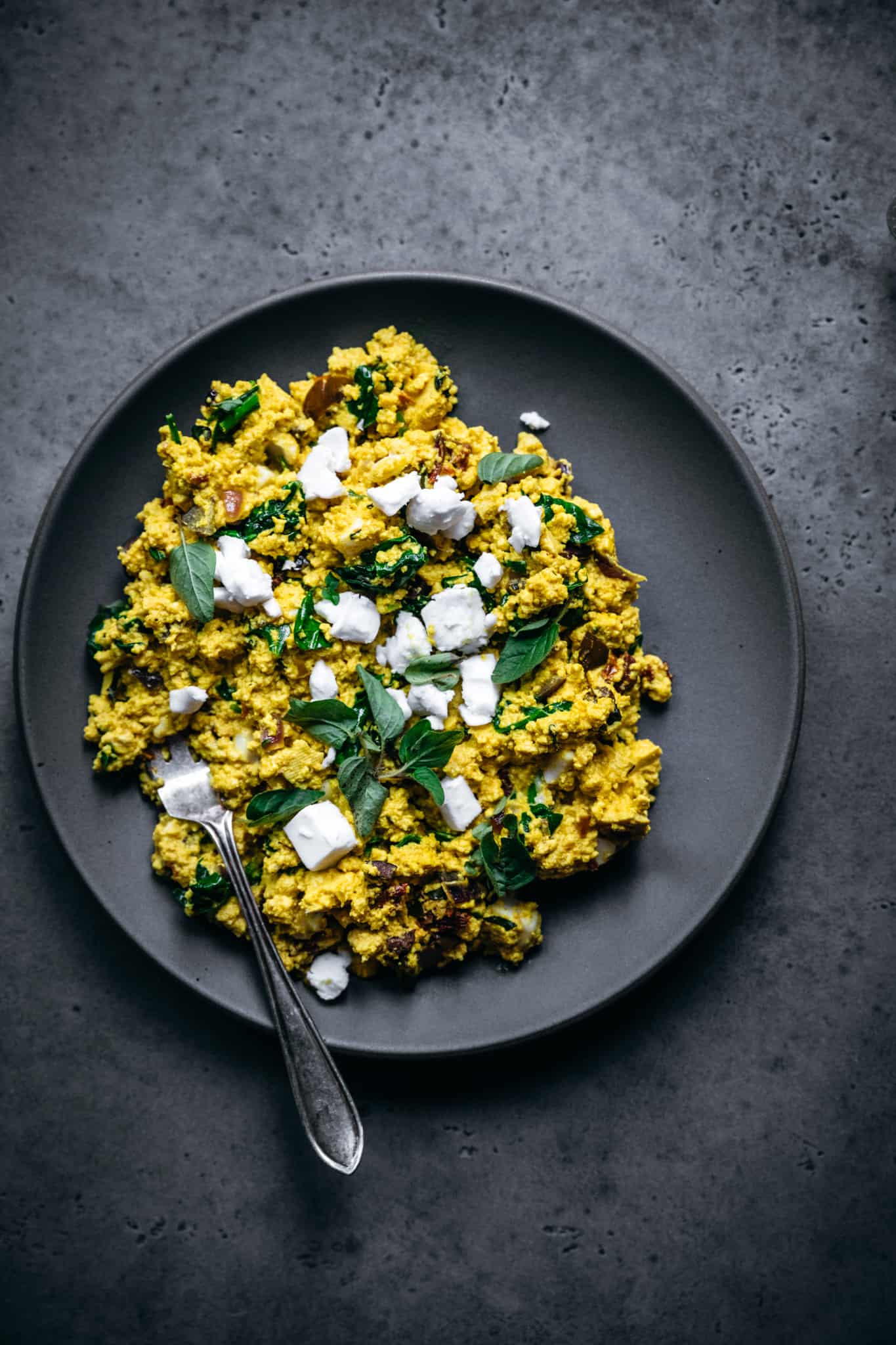 overhead view of greek scrambled tofu on grey plate with fork