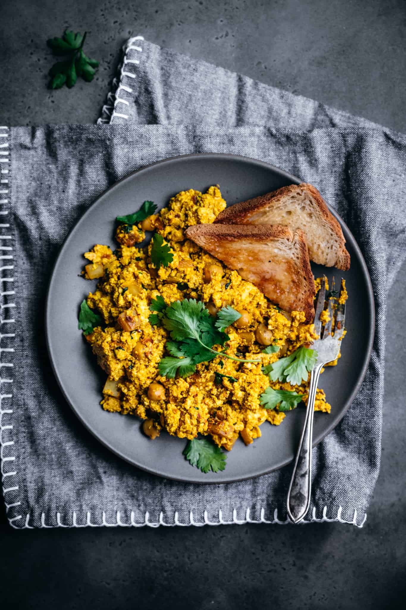 overhead view of curry-spiced vegan scrambled tofu on a grey plate with toast and fresh cilantro