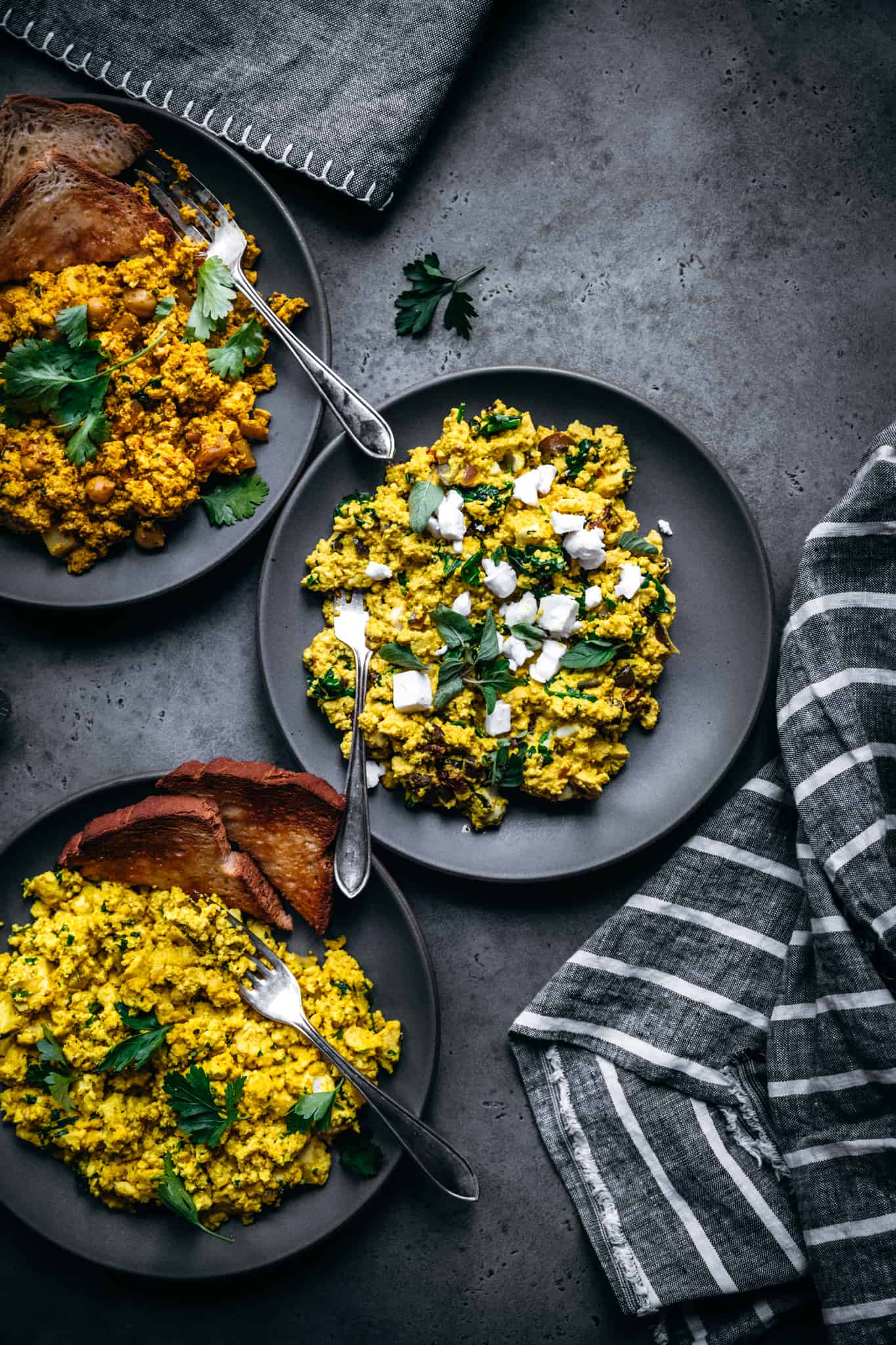 overhead view of 3 plates of vegan scrambled todu with fresh herbs and cheese