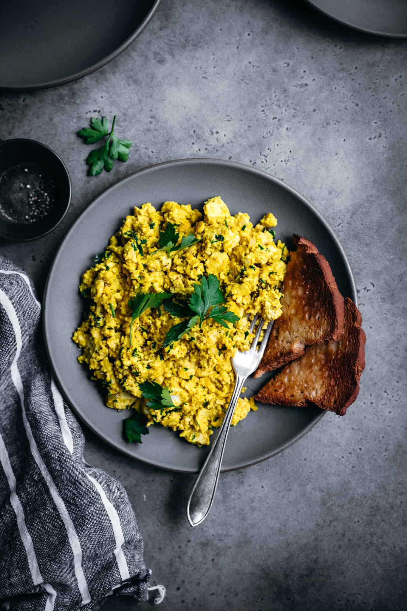 overhead view of cheesy herbed vegan tofu scrambled eggs on a plate with toast