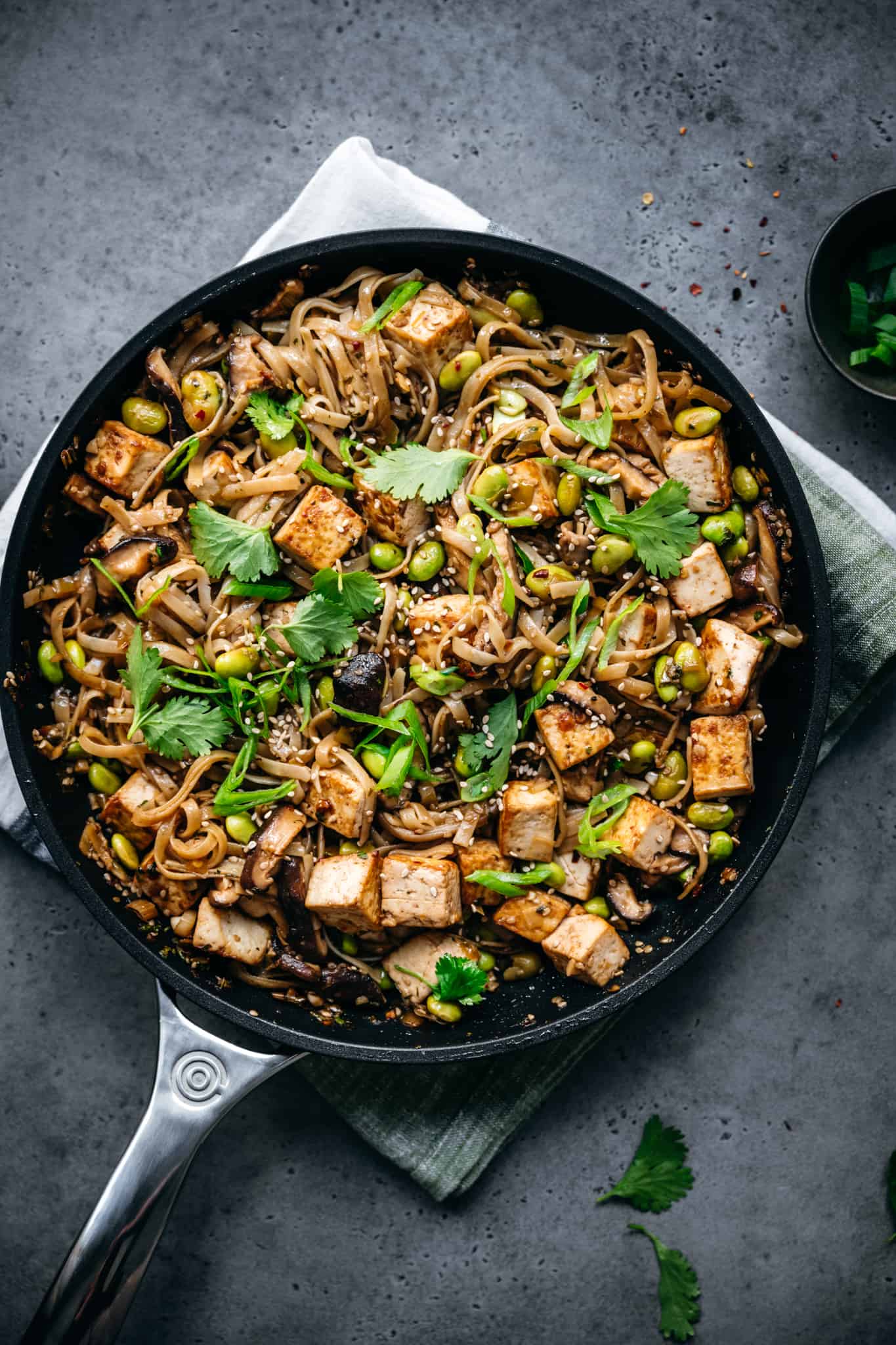 vegan rice noodles with tofu, edamame and scallions in a nonstick pan