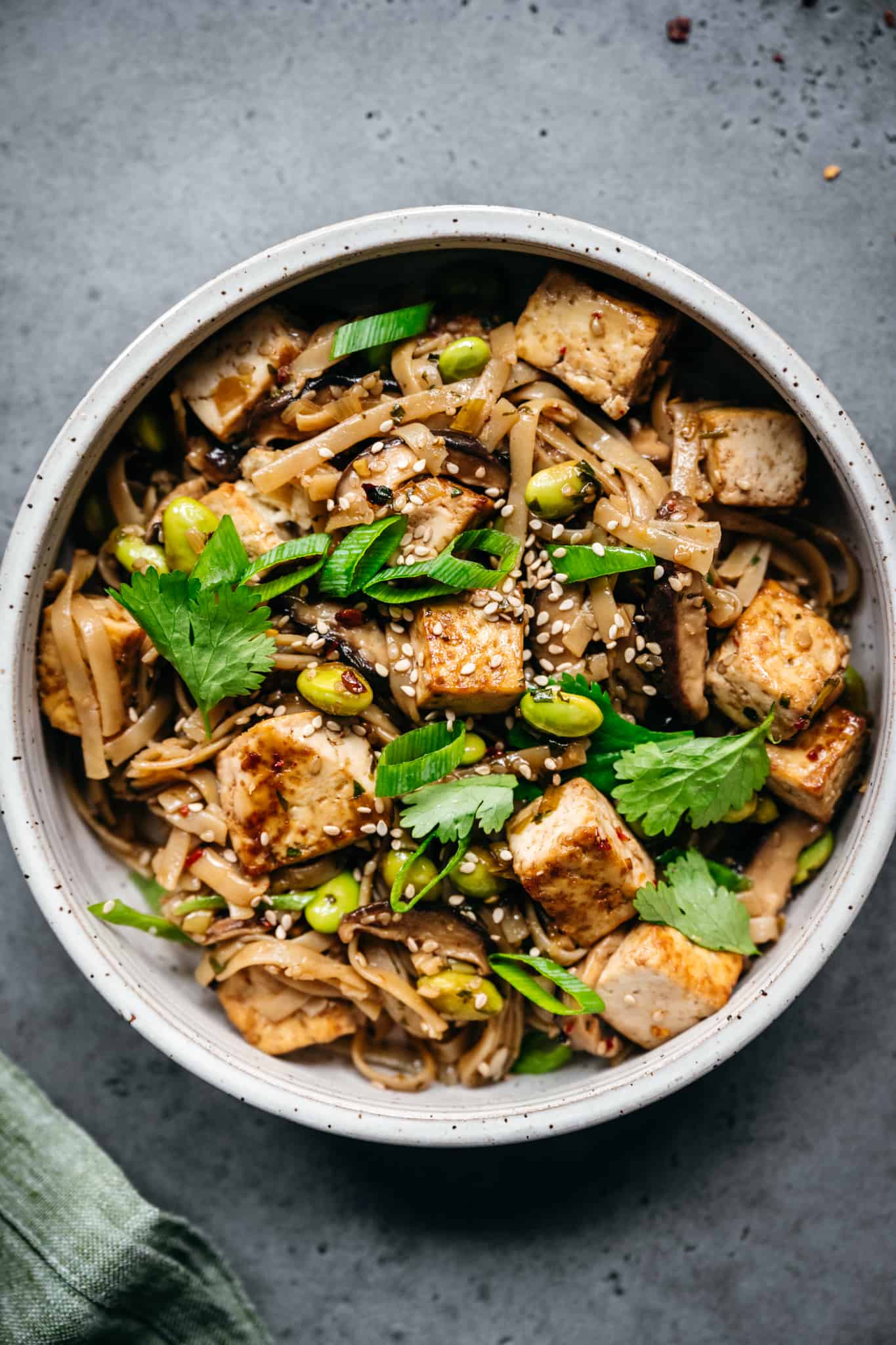 close up view of vegan rice noodles with crispy tofu, mushrooms and edamame in white bowl