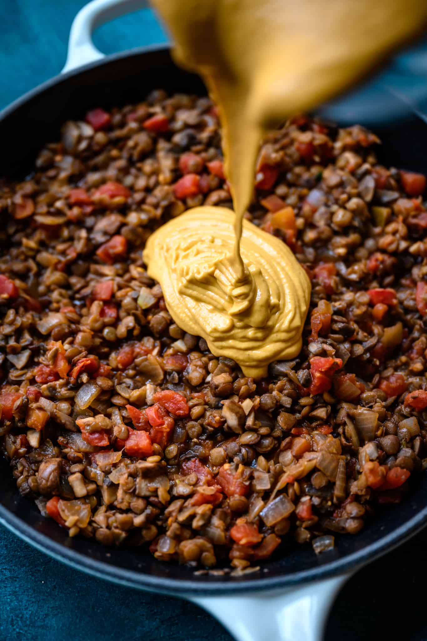 pouring vegan queso dip into vegan lentil mushroom mixture