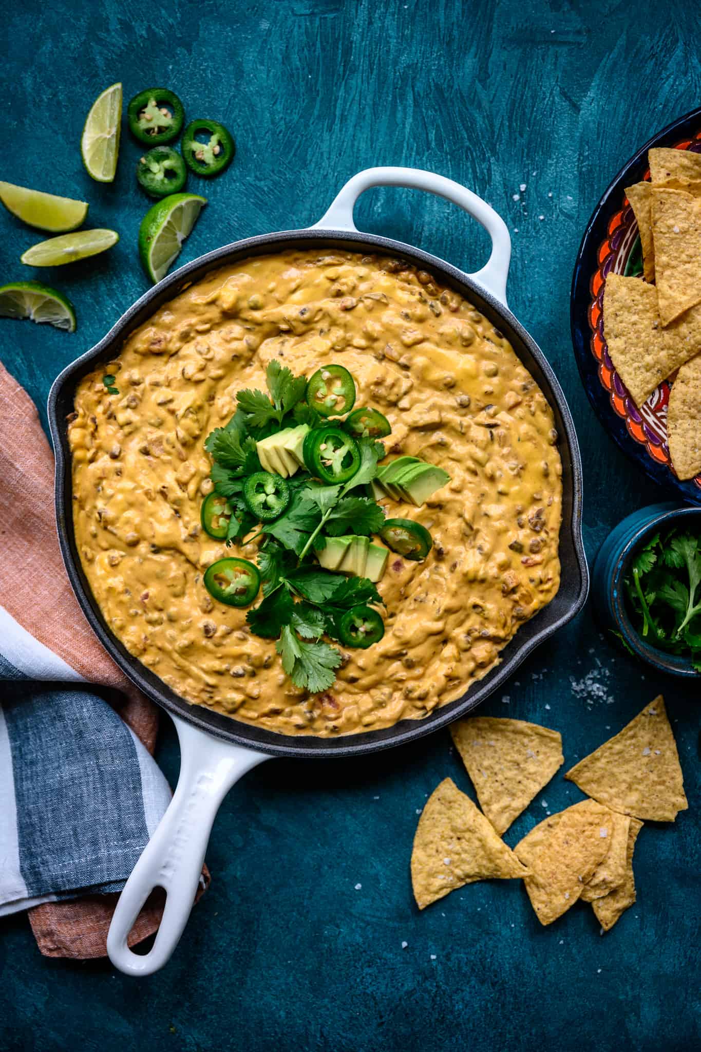 overhead view of vegan chile con queso dip with tortilla chips in skillet on blue background