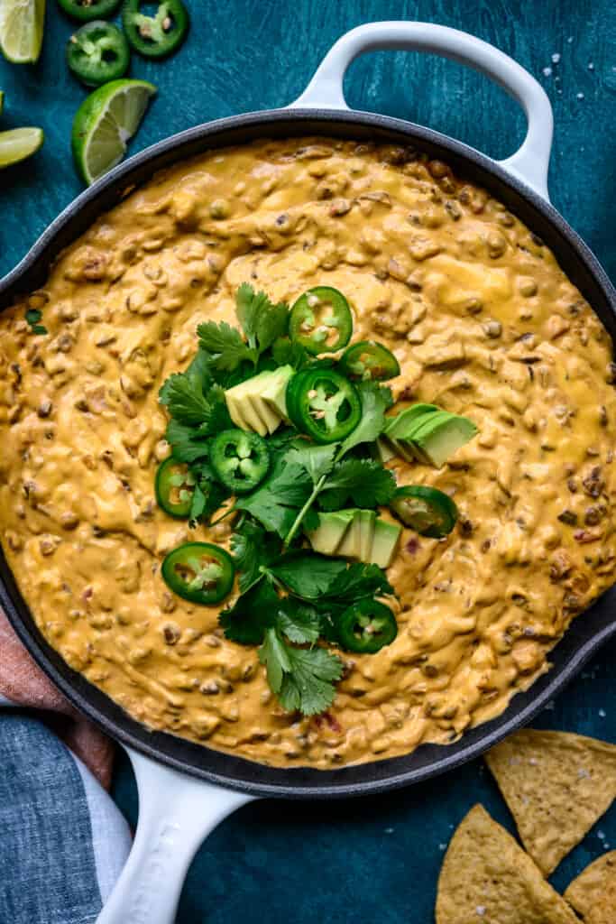 close up overhead view of vegan chile con queso topped with avocado, cilantro and jalapeño