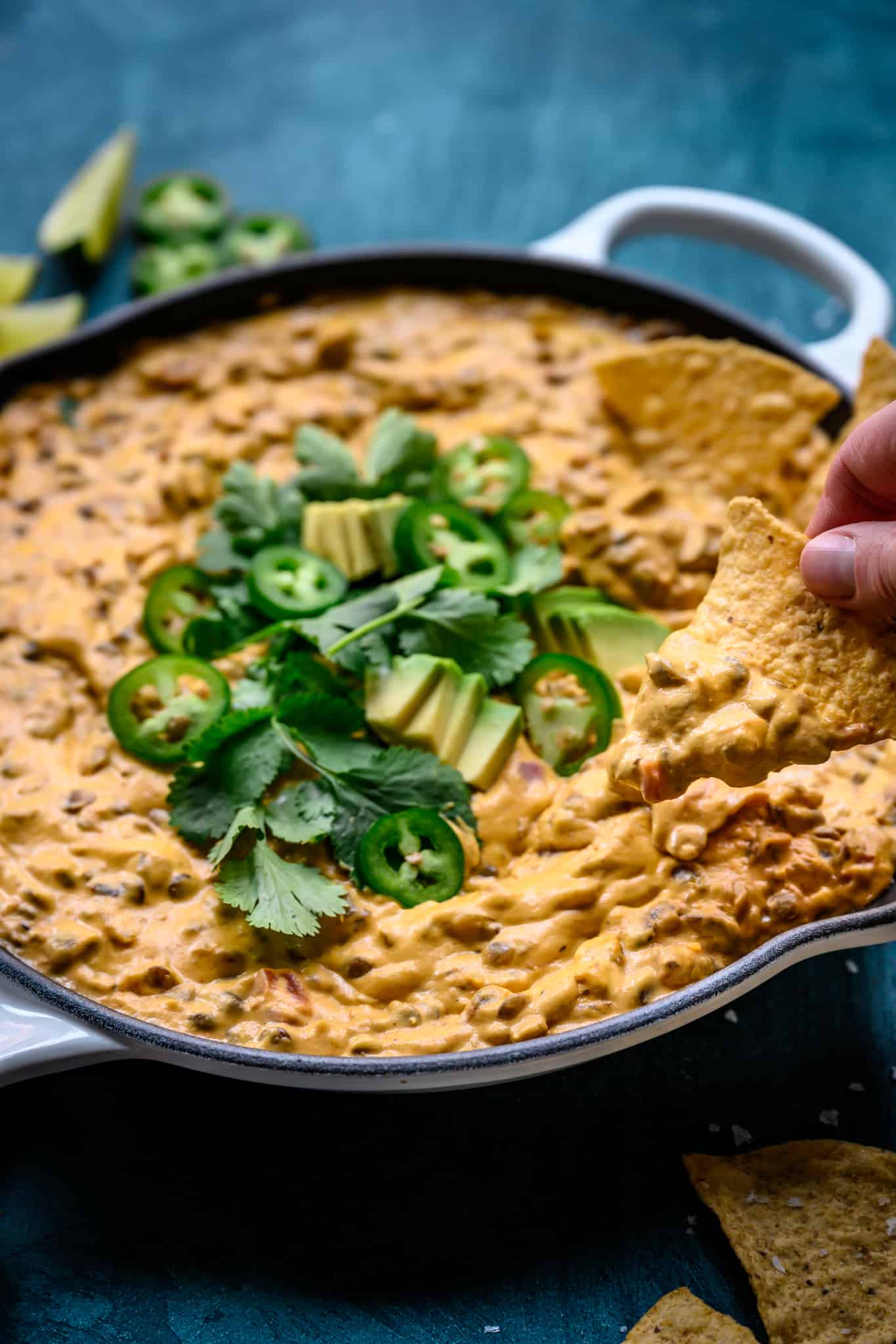 side view of person dipping tortilla chip into vegan chile con queso dip