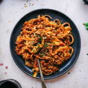 overhead view of vegan lentil bolognese sauce over pasta on black plate with fork.