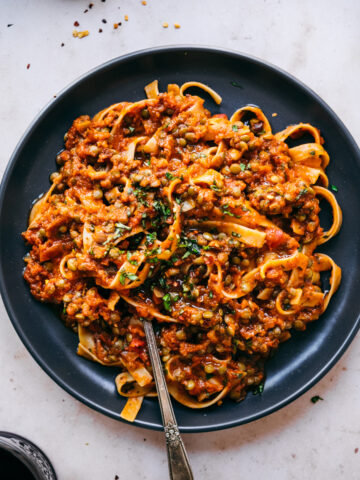 overhead view of vegan lentil bolognese sauce over pasta on black plate with fork.