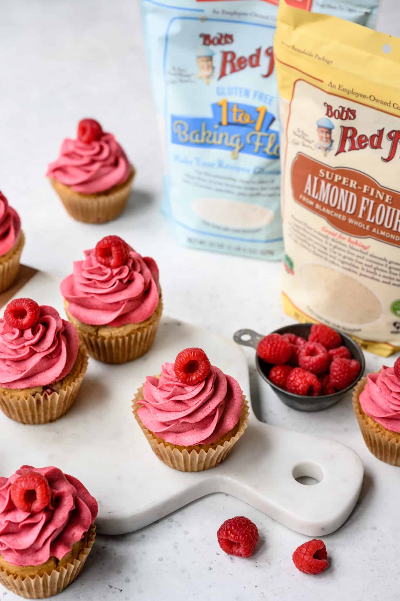 side view of raspberry almond cupcakes on white background with Bob's Red Mill products