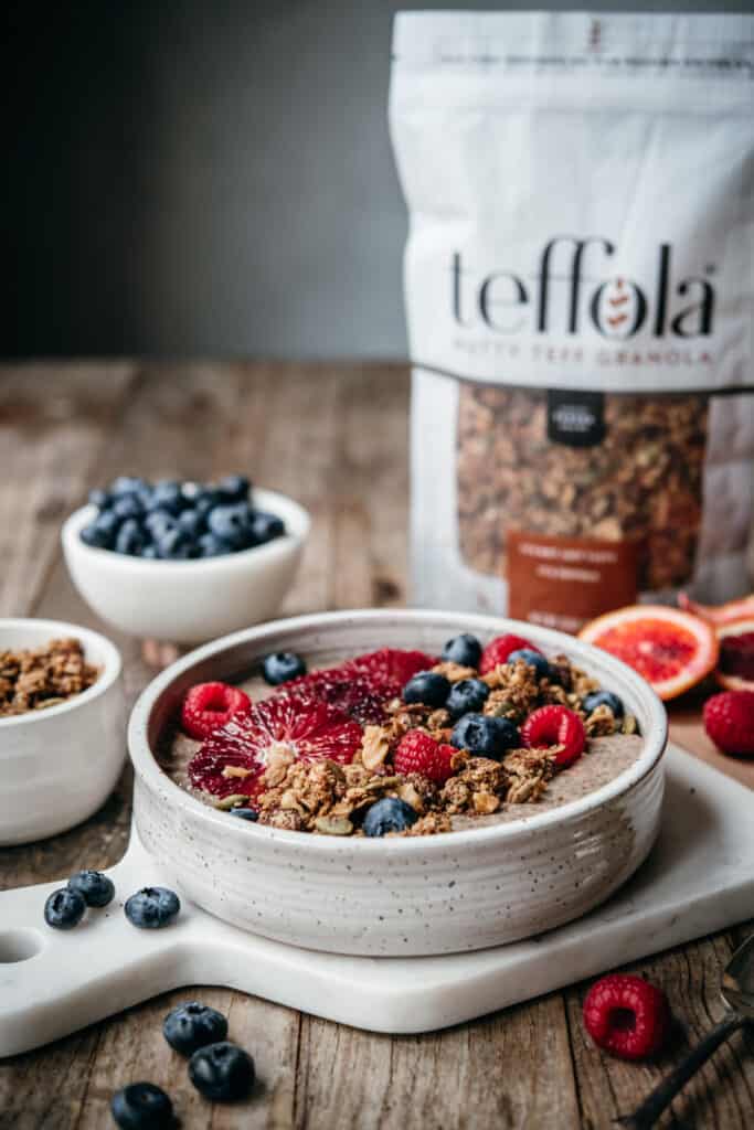 side view of chai chia pudding in bowl with berries, blood orange slices and granola on wood table