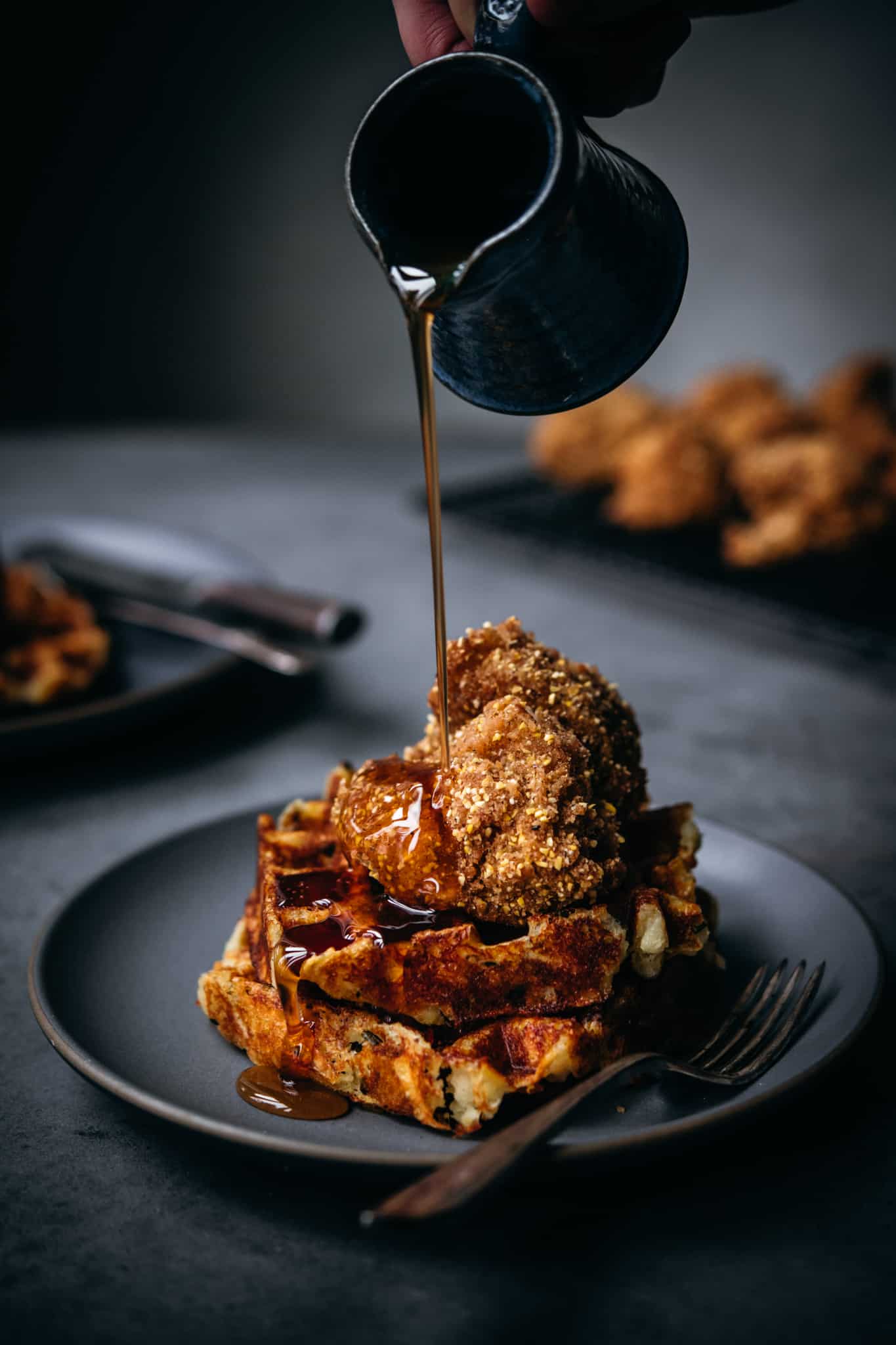 side view of pouring maple syrup onto vegan chicken and waffles