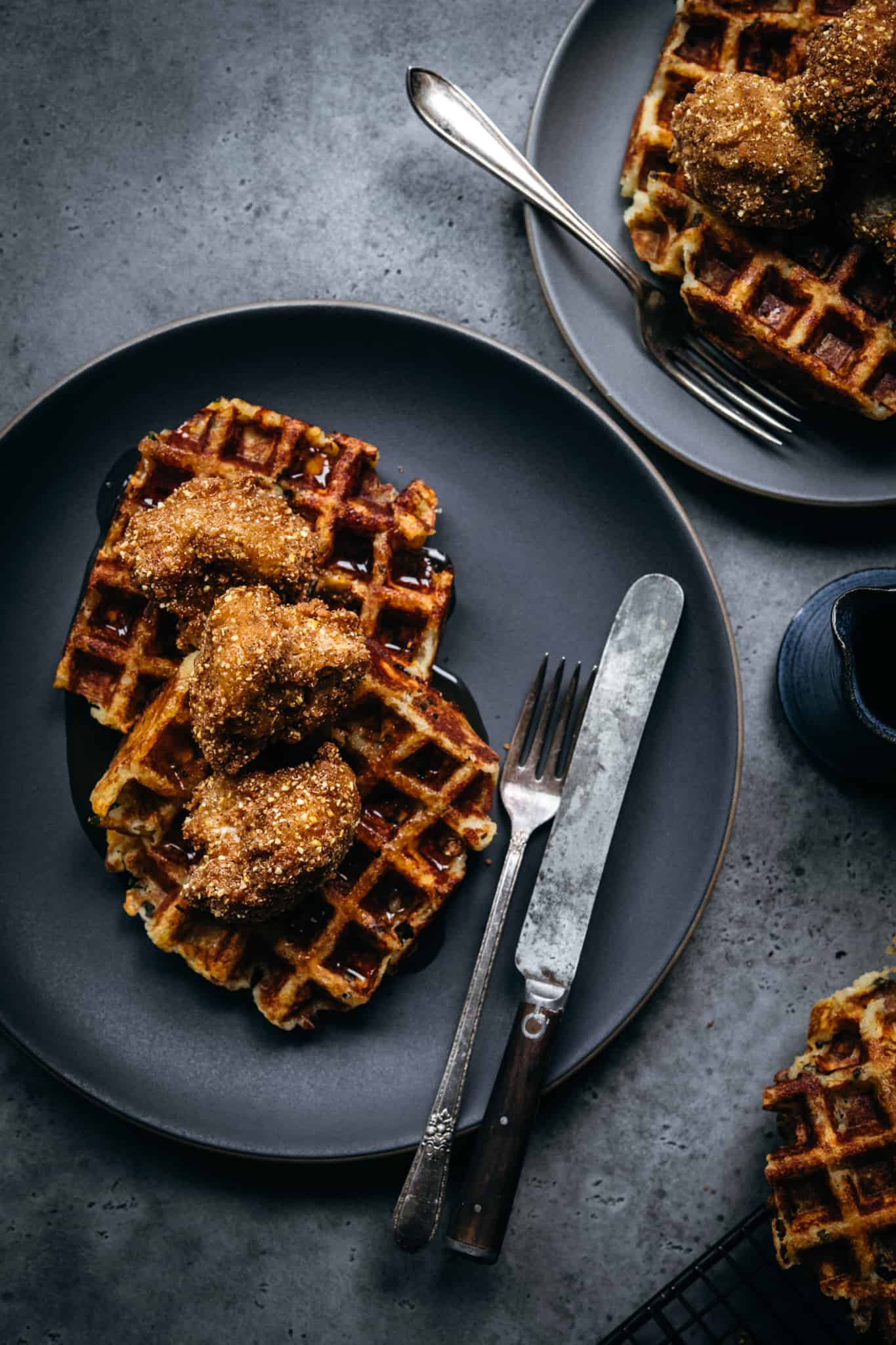 overhead view of vegan chicken and waffles on grey plate with hot maple syrup and fork