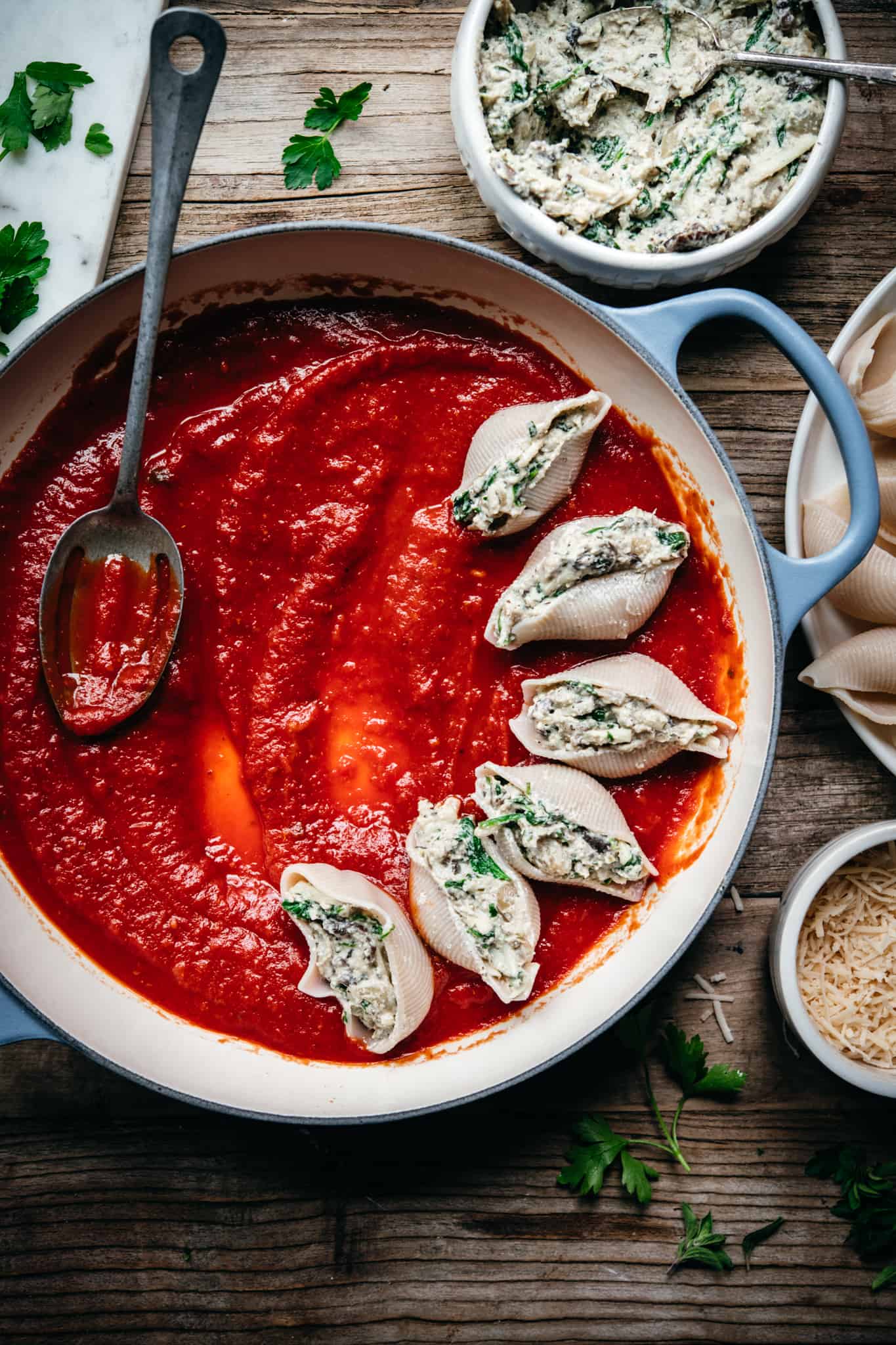 adding stuffed shells to circular pan with marinara sauce